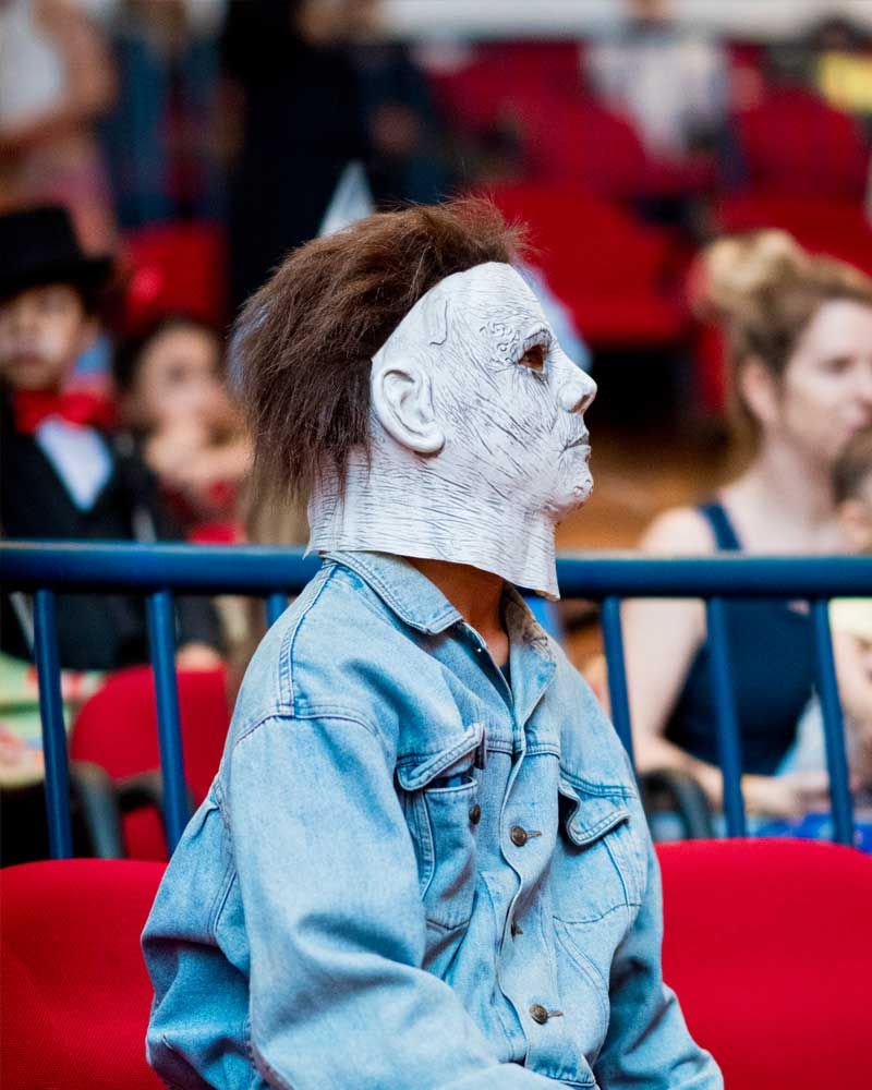 A man wearing a mask and a denim jacket is sitting on a red bench.
