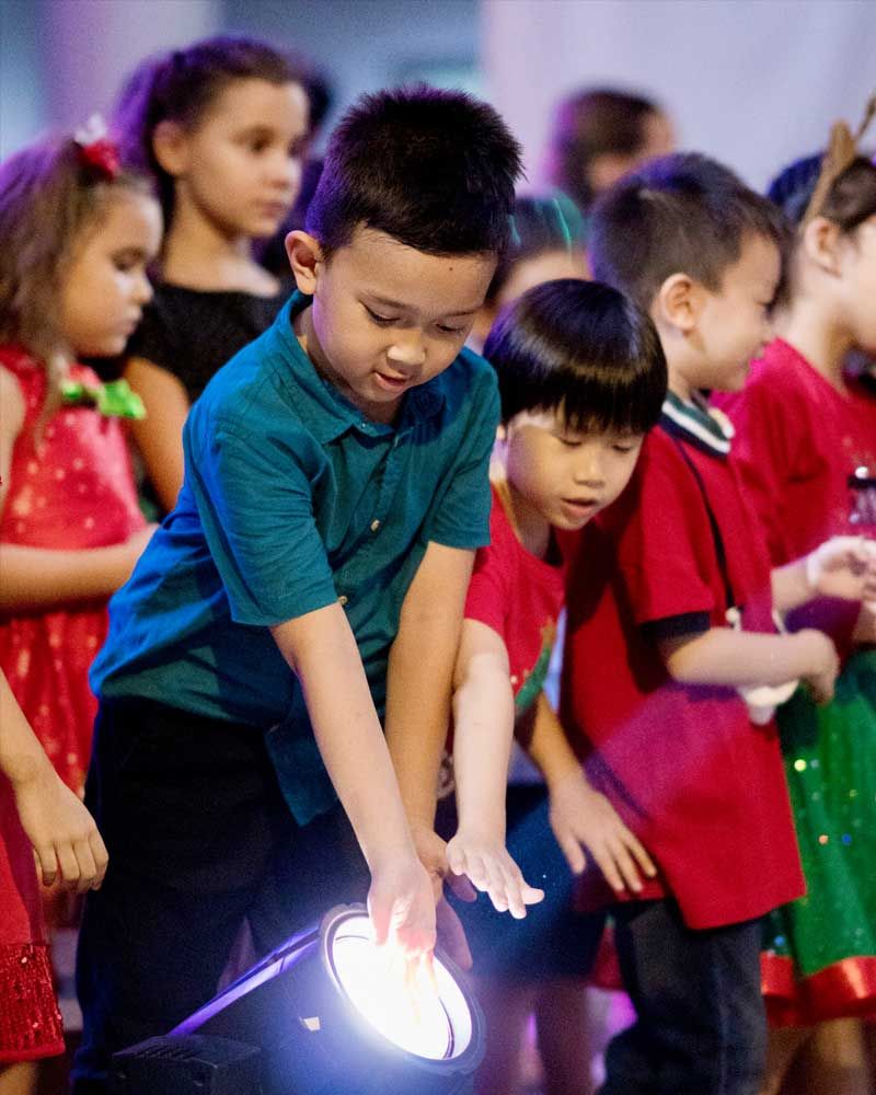 A boy in a blue shirt is holding a light in front of a crowd of children.