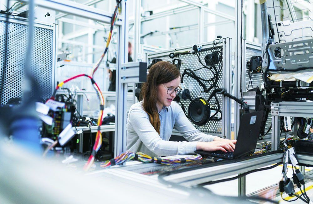 A woman is working on a laptop computer in a factory.