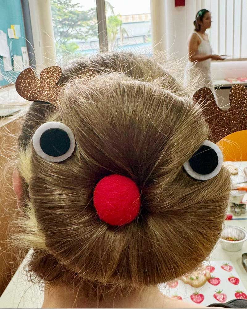 A woman is wearing a bun with googly eyes and a red nose.