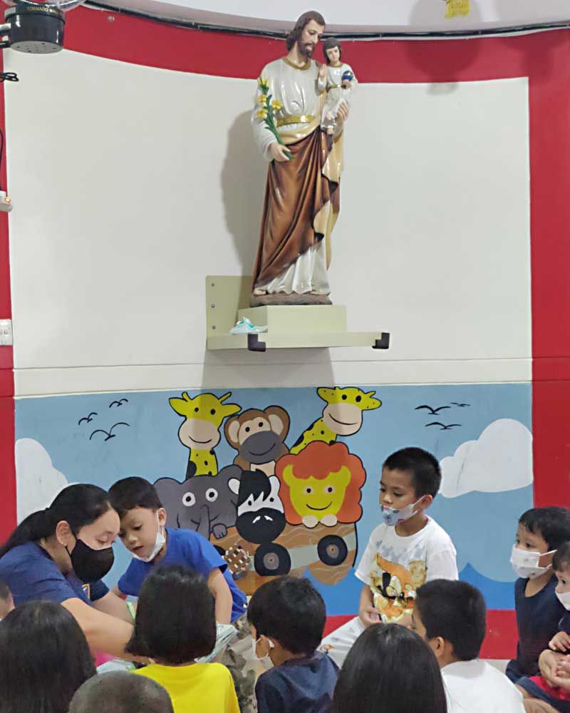 A group of children are sitting in front of a statue of jesus