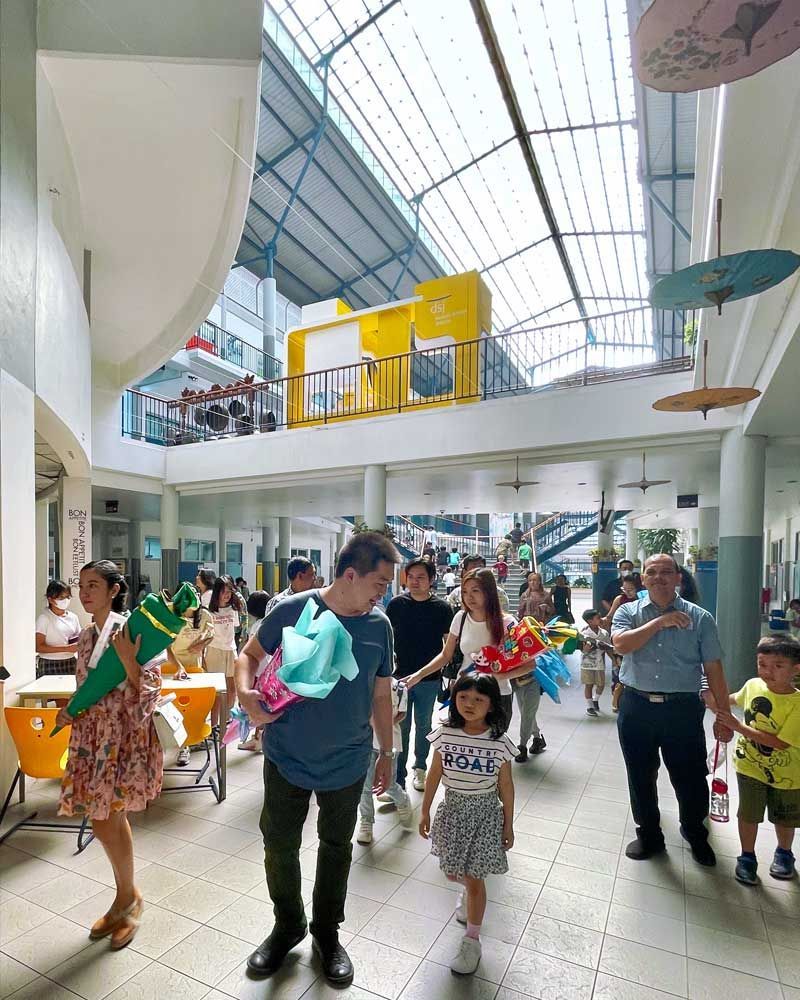 A group of people are walking through a building with umbrellas hanging from the ceiling.