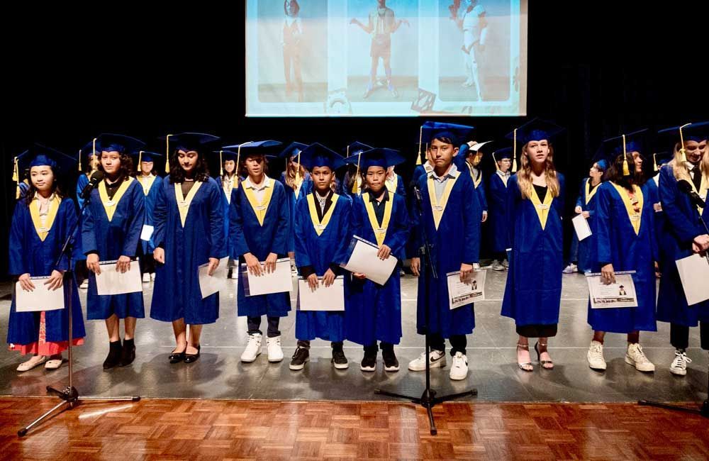 A group of graduates are standing on a stage singing into microphones.