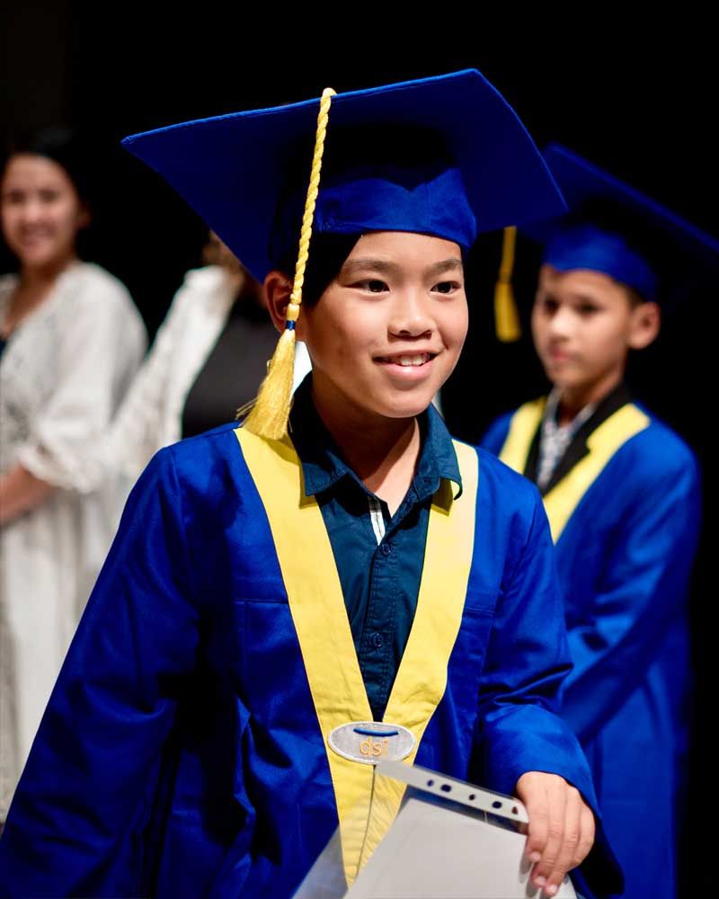 A young boy in a graduation cap and gown is holding a diploma.