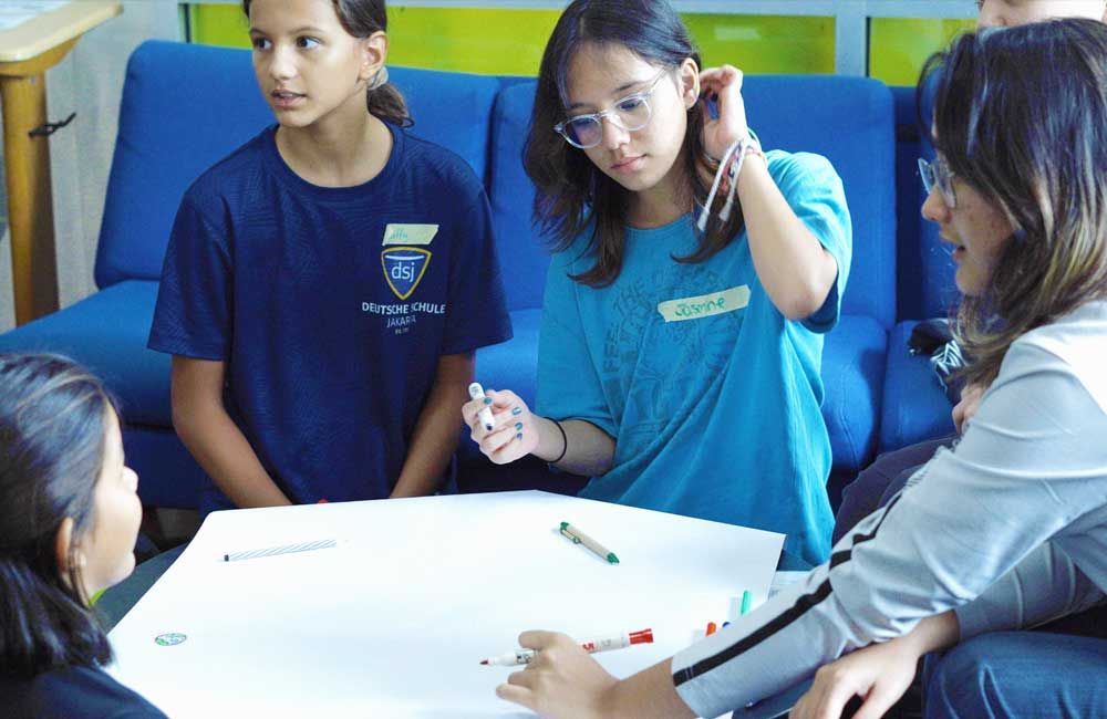 A group of young girls are sitting around a table with markers on it