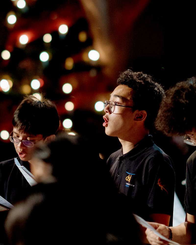 A group of young men are singing in a choir in front of a christmas tree.