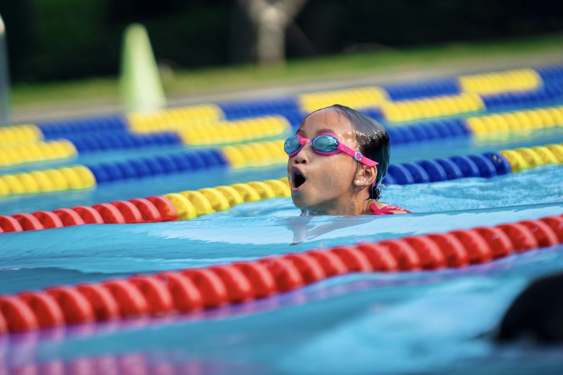 A young girl is swimming in a swimming pool wearing goggles.