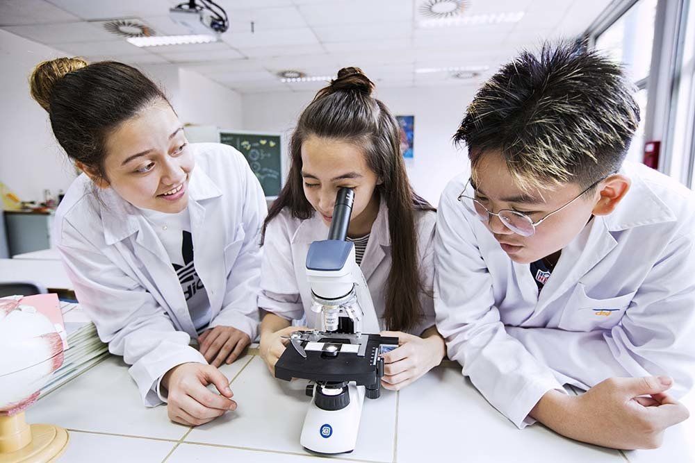 Three secondary students working with a microscope during biology class at the german School Jakarta