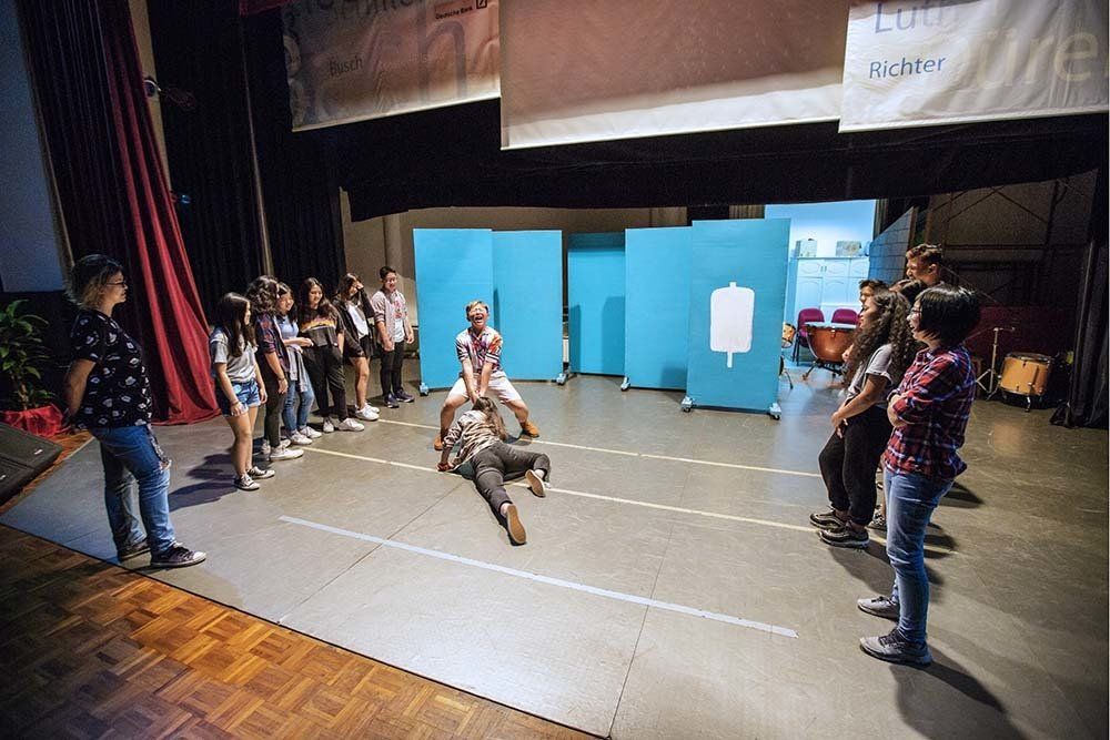 A group of people are standing around a stage with a man laying on the floor.
