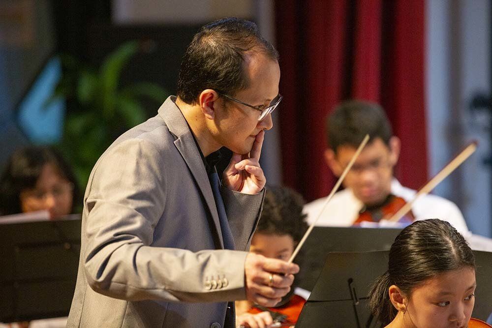 A man is standing in front of a group of people playing violins.