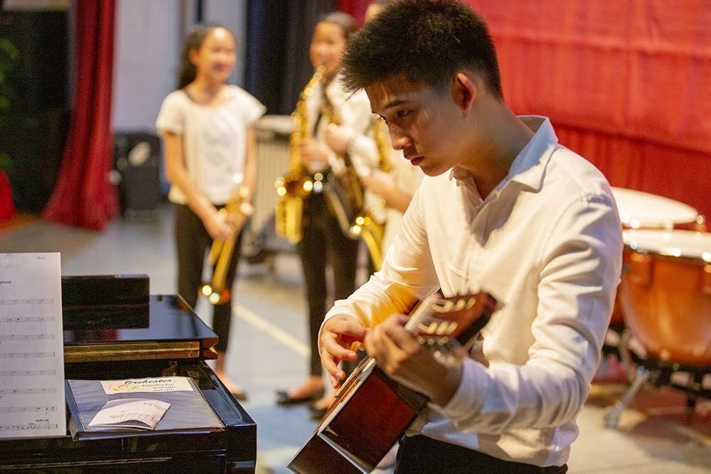 A young man is playing a guitar in front of a group of people.