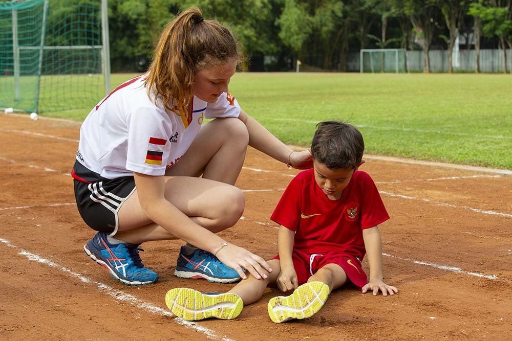 An older German School Jakarta student helps a younger boy who fell on the running track