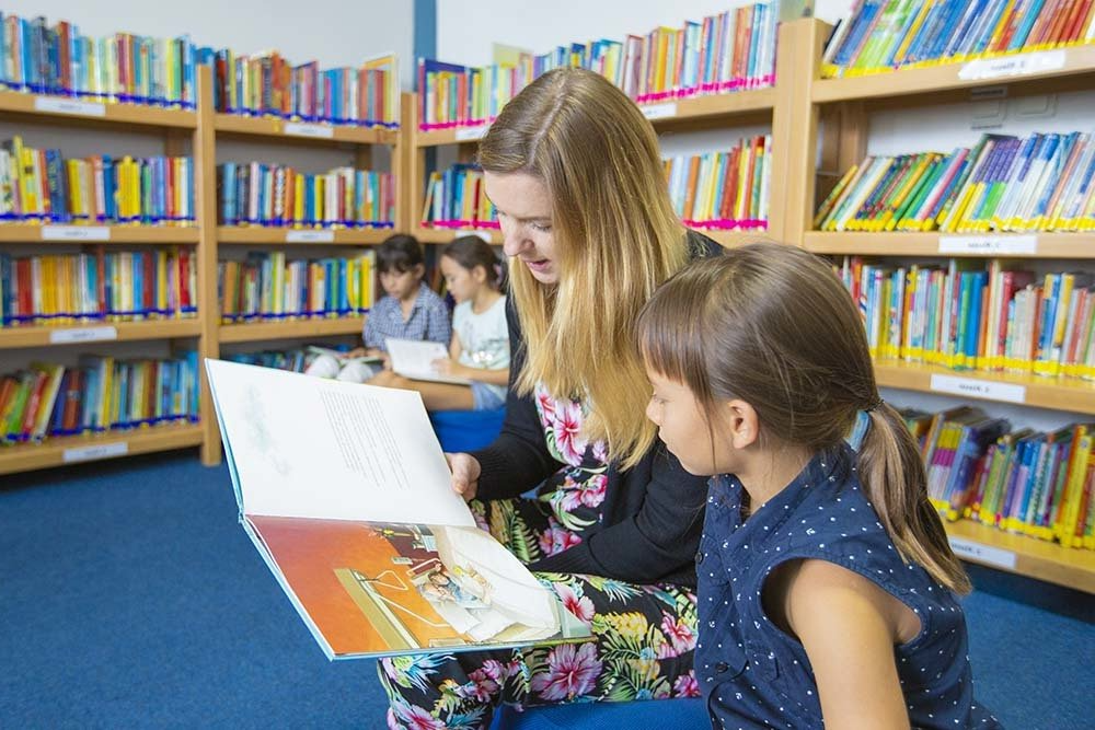 A woman is reading a book to a little girl in a library.