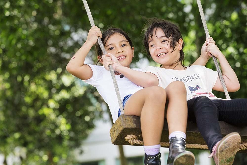 A boy and a girl are sitting on a wooden swing.