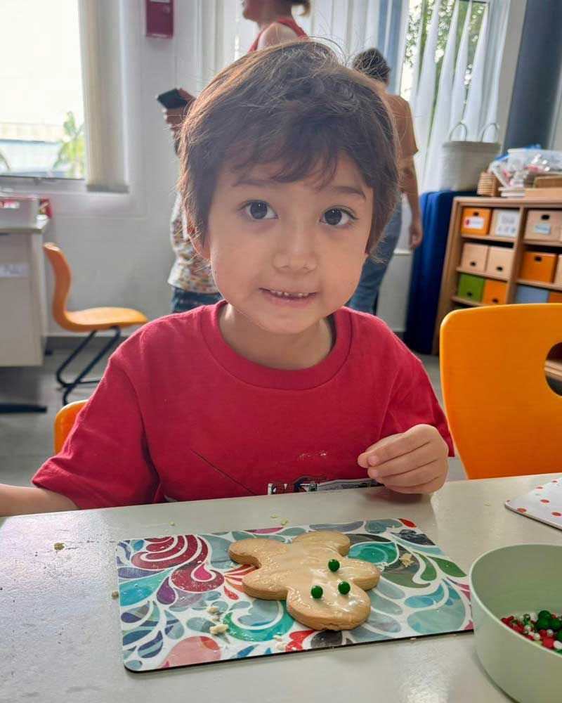 A young boy is sitting at a table decorating a gingerbread man cookie