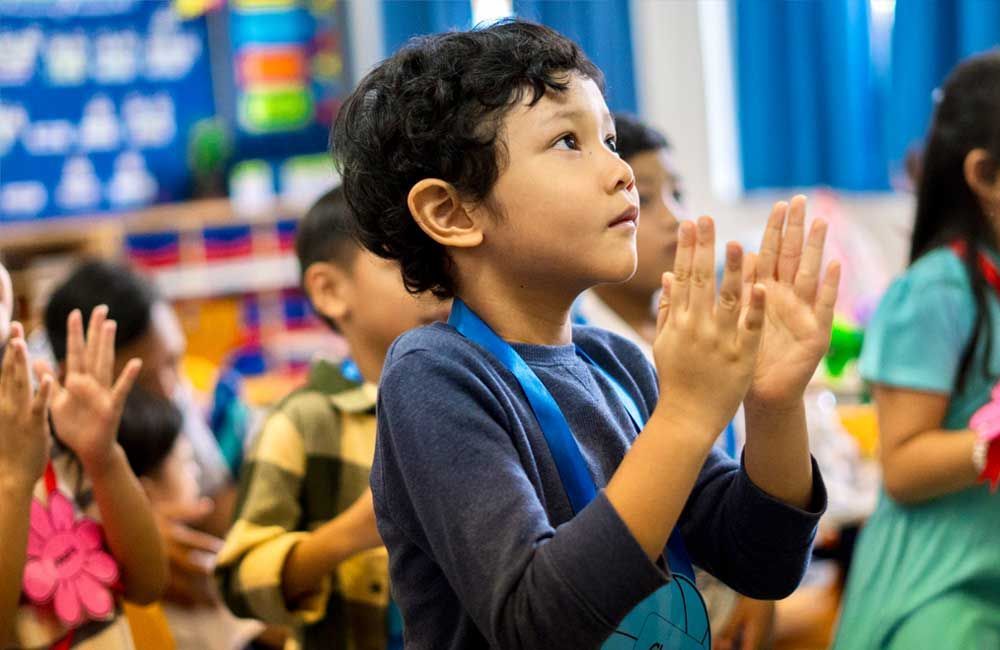 A group of children are clapping their hands in a classroom.