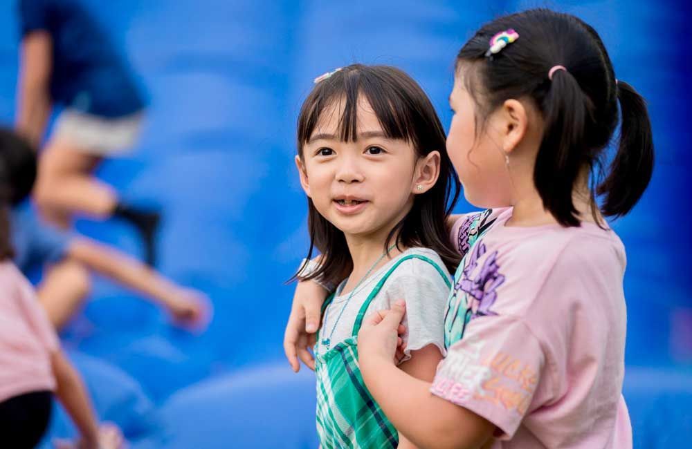 Two little girls are standing next to each other in front of a blue wall.