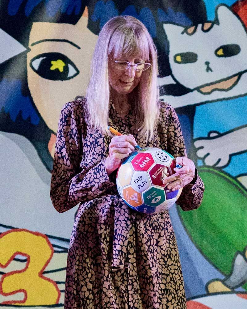 A woman is holding a soccer ball in front of a painting of a woman and a cat.