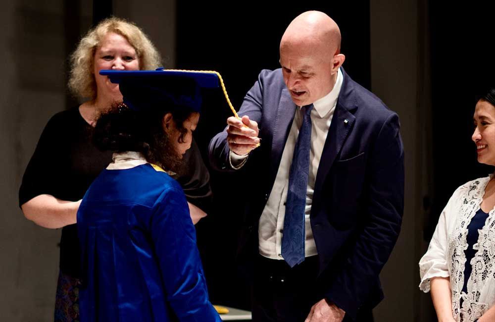 A man in a suit is giving a diploma to a woman in a graduation cap and gown.