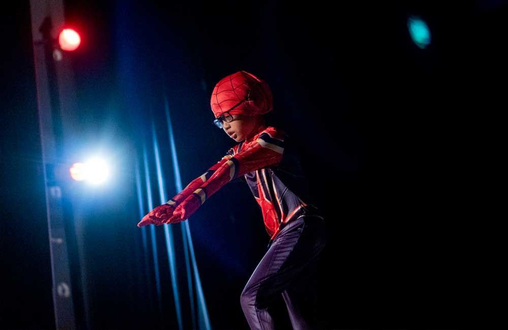 A young boy in a spiderman costume is standing on a stage.