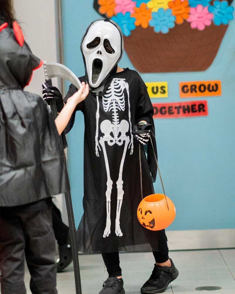 A child in a skeleton costume holds an orange bucket