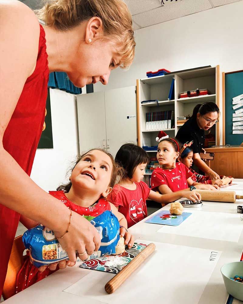 A woman is teaching a group of children how to bake in a classroom.