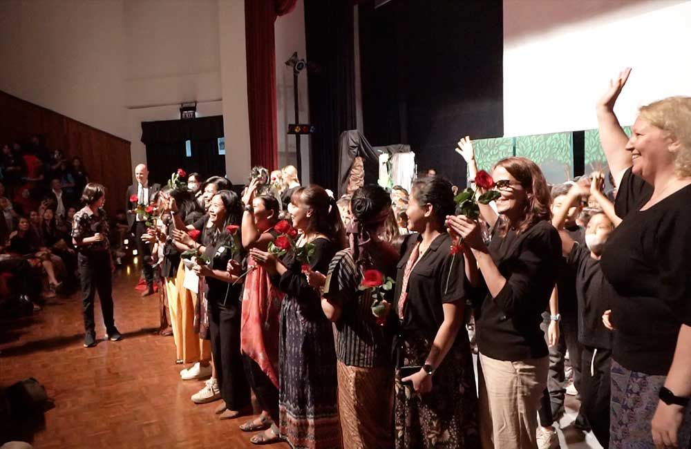 A group of people are standing on a stage holding flowers.