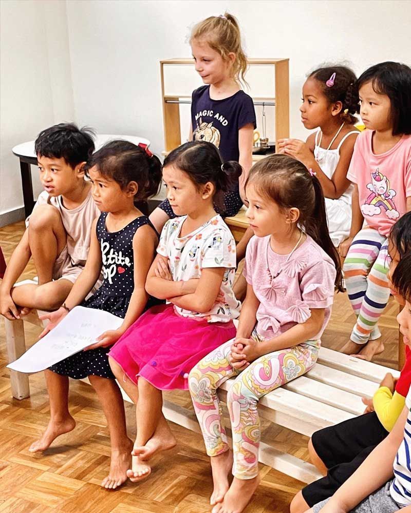 A group of children are sitting on benches in a room.
