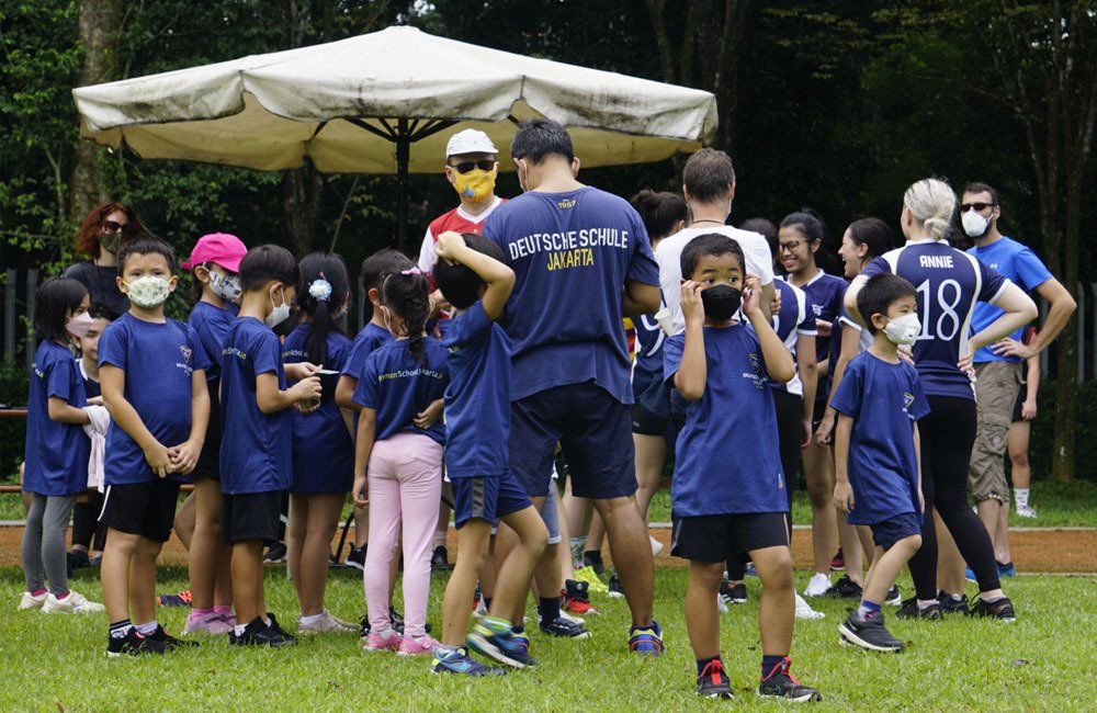 A group of children wearing face masks are standing in a field.