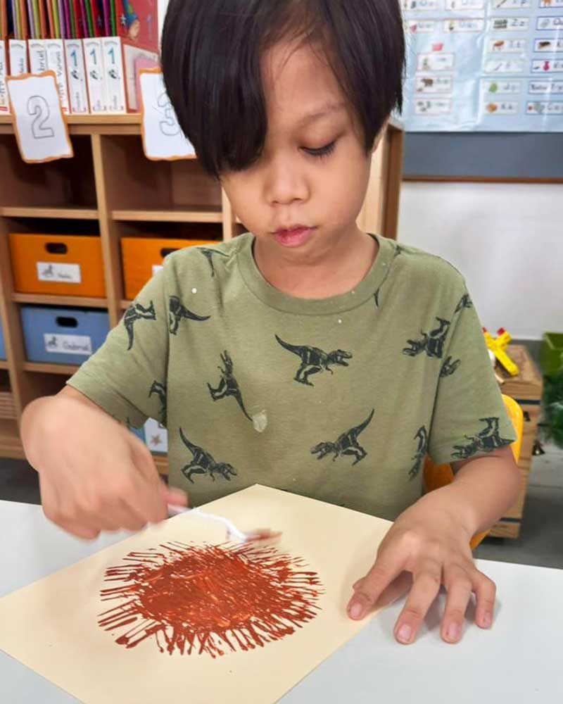 A young boy is painting a sun on a piece of paper