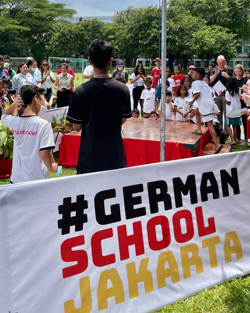 A man stands in front of a sign that says german school jakarta