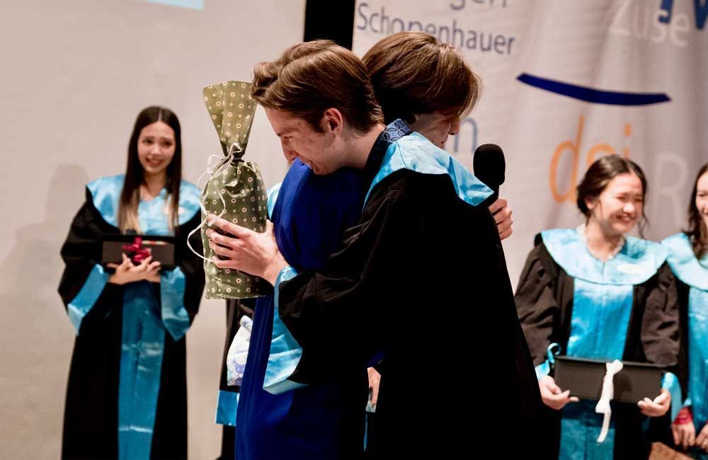 A group of people in graduation gowns are hugging each other.