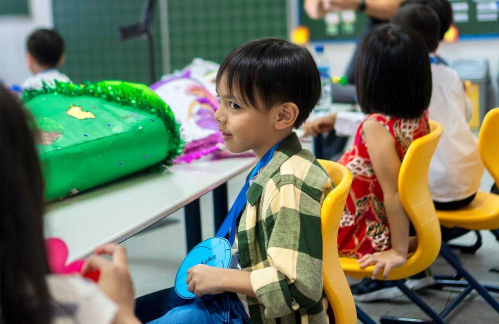 A young boy is sitting in a classroom with other children.