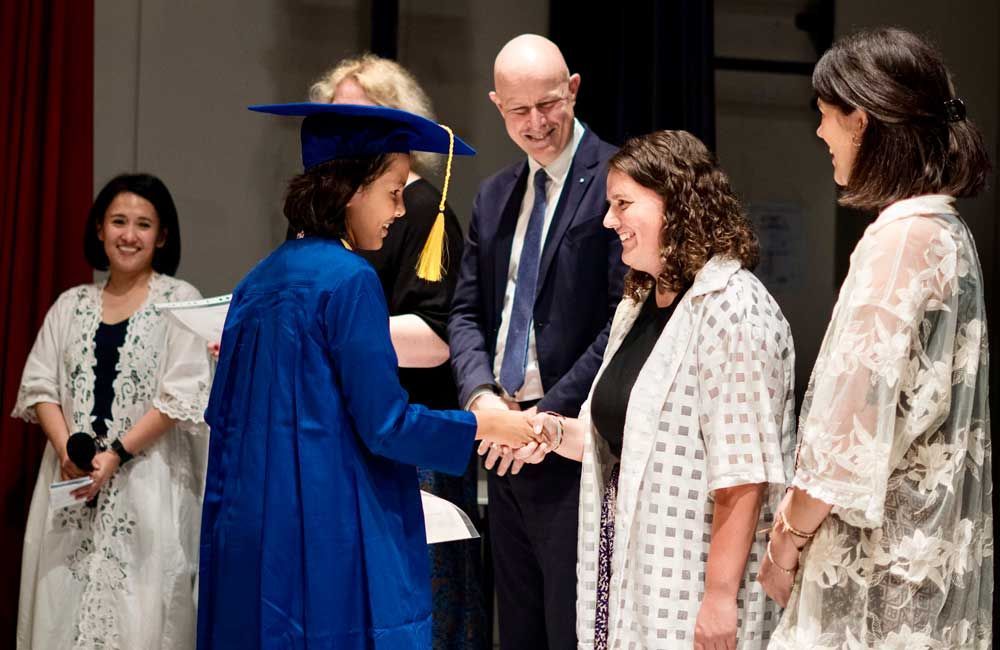 A woman in a blue cap and gown is shaking hands with a man in a suit.