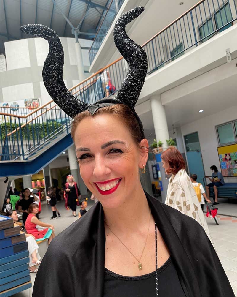 A woman wearing a black cape and horns is smiling.