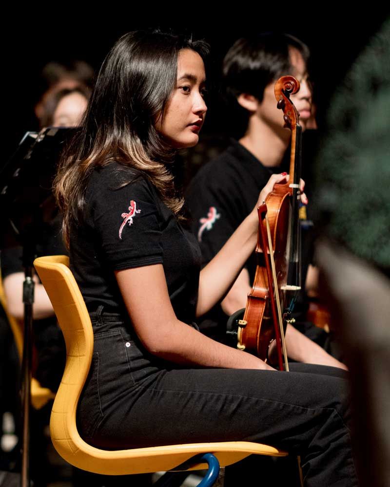 A woman is sitting in a yellow chair playing a violin