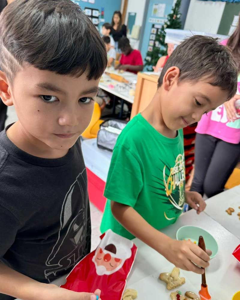 Two young boys are decorating christmas cookies in a classroom