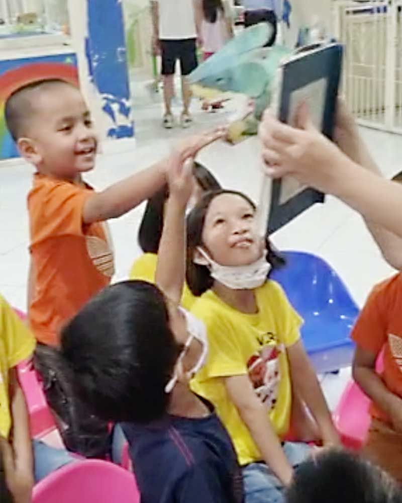 A group of children are sitting in chairs and playing with a book.