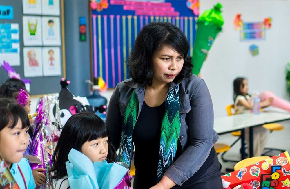 A woman is standing in front of a group of children in a classroom.