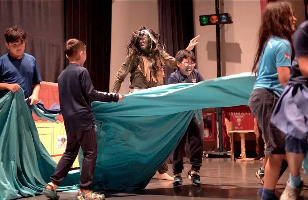 A group of children are playing with a blue cloth on a stage.