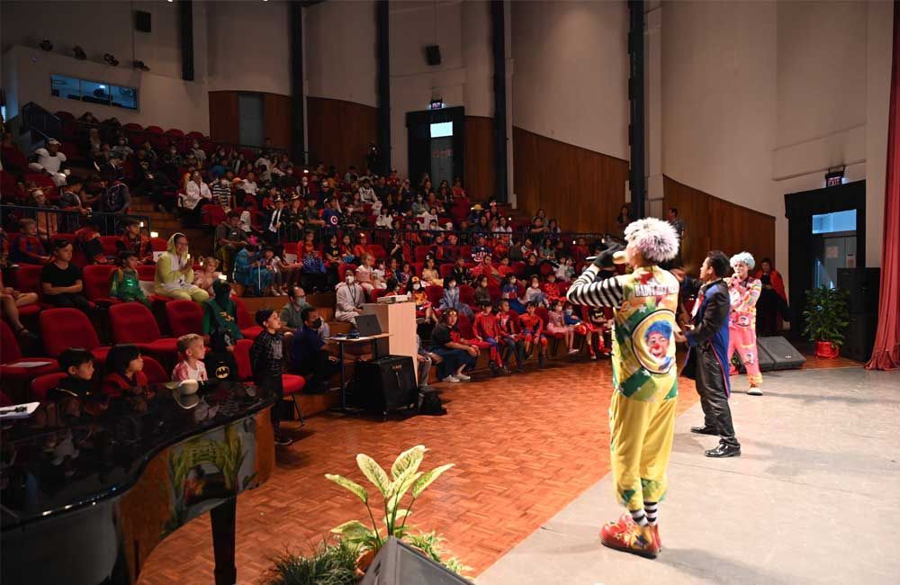 A group of people in colorful costumes perform on stage in a large auditorium