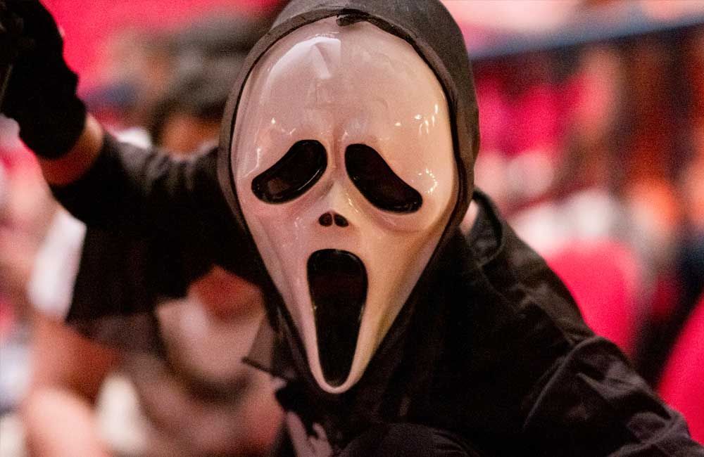 A person is wearing a scream mask and a black hoodie.