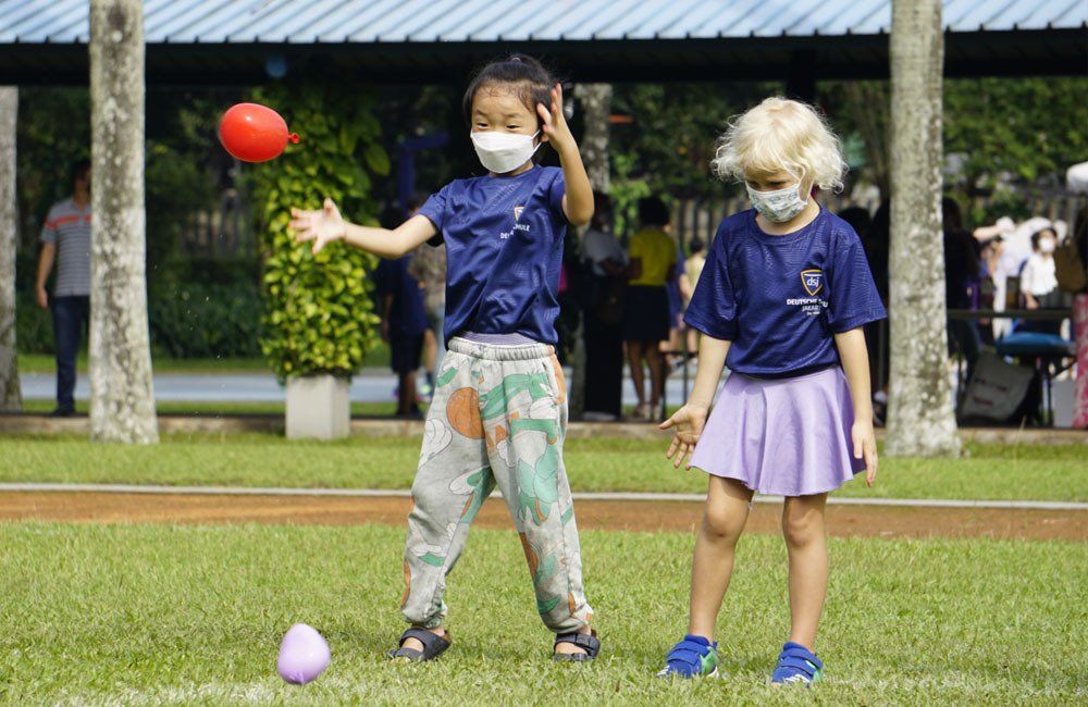 Two young girls wearing face masks are playing with a ball.