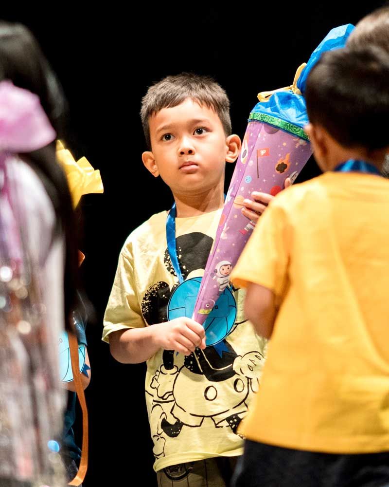 A young boy in a yellow shirt is holding a purple cone.