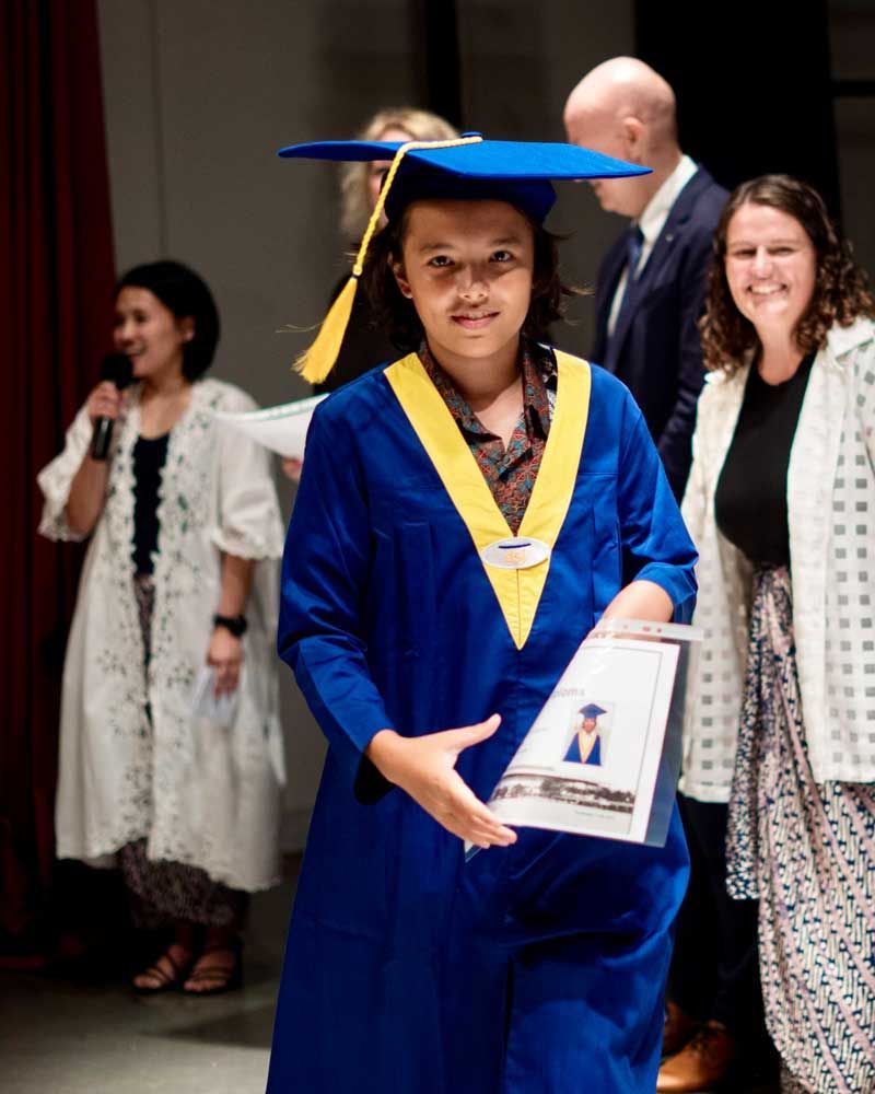 A young girl in a graduation cap and gown is holding a diploma.