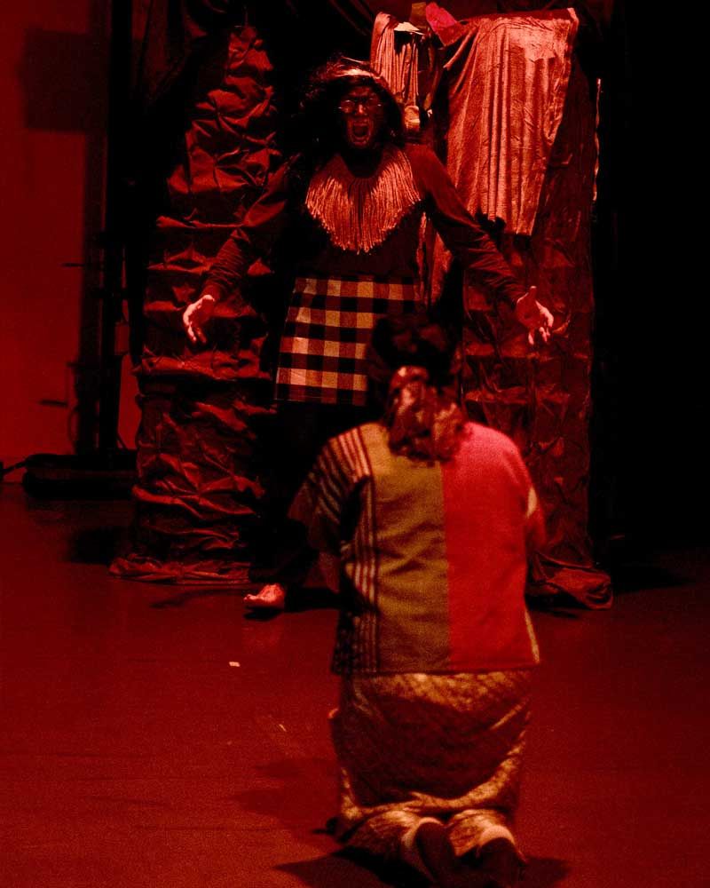 A man in a clown costume is kneeling down in front of a man in a plaid shirt.