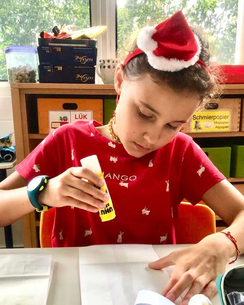 A young girl wearing a santa hat is sitting at a table using glue.