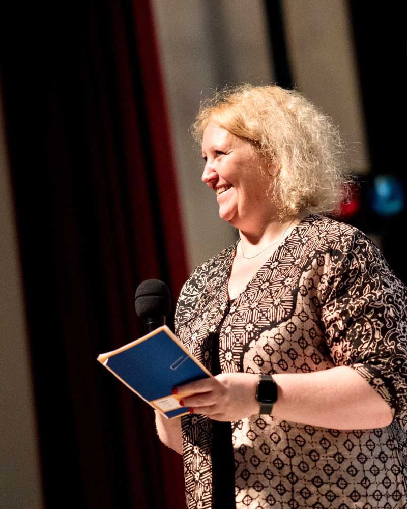 A woman is smiling while holding a book in front of a microphone.