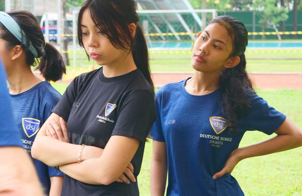 A group of girls wearing blue shirts are standing on a field.