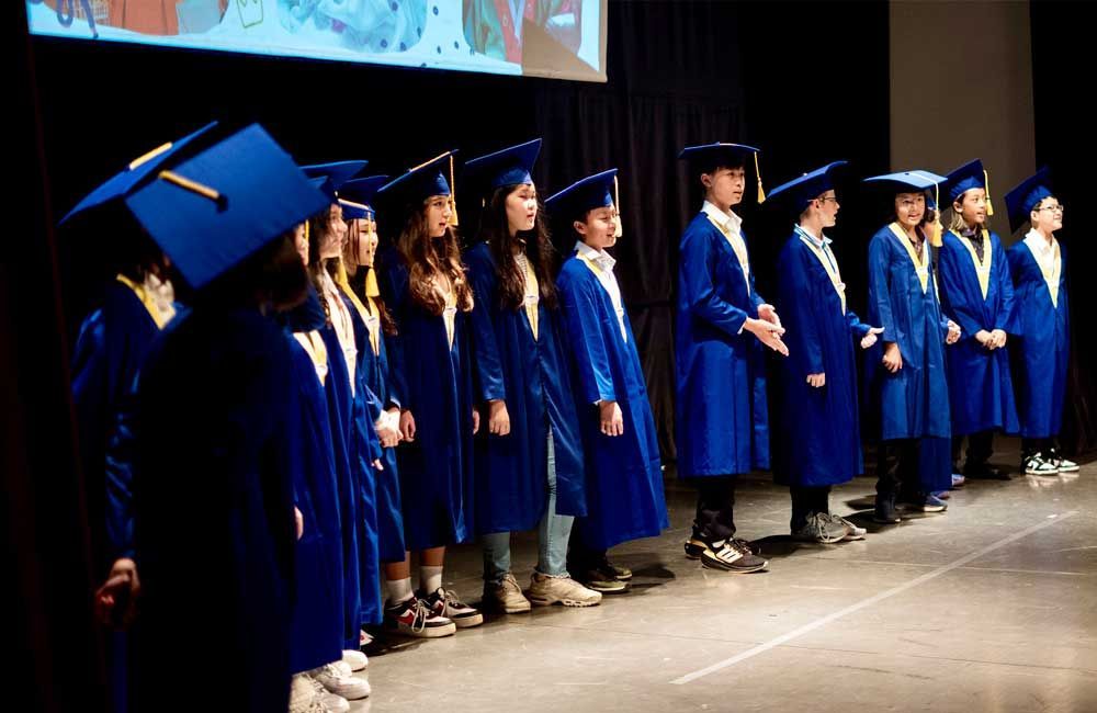 A group of children wearing graduation caps and gowns are standing on a stage.